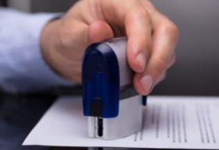 Hand stamping official document – representing NRIWAY’s trusted attestation and verification services for NRIs.